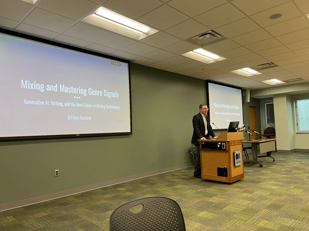 Bill Hart-Davidson stands at a podium in front of two screens, which display a slide that reads "Mixing and Mastering Gnre Signals"