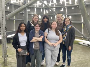 6 students and instructor standing inside a metal sculpture, posing for the camera